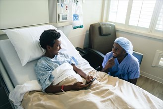 Black nurse talking to boy in hospital bed