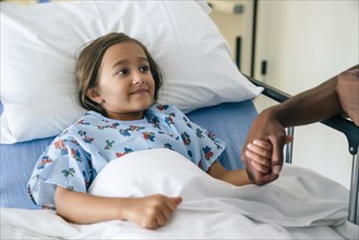 Man holding hands with girl in hospital bed