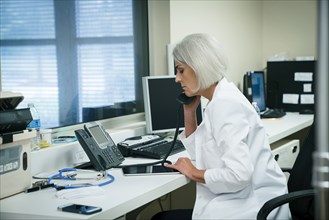 Caucasian doctor talking on telephone and using digital tablet