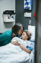 Mother kissing forehead of daughter in hospital bed