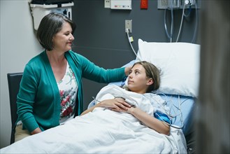 Mother comforting daughter in hospital bed