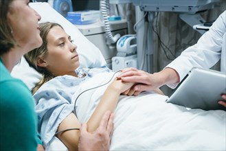 Caucasian doctor with digital tablet comforting girl in hospital bed