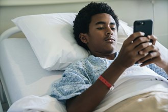 Black boy laying in hospital bed texting on cell phone