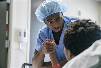 Black doctor holding hand of boy in hospital bed