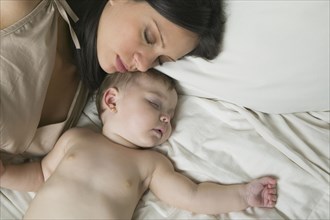 Hispanic mother and baby sleeping on bed