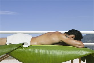 Asian man laying on spa table with banana leaves outdoors