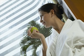 Hispanic woman in spa bathrobe holding apple