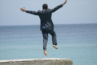 Hispanic businessman jumping off dock