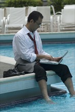 Hispanic businessman using laptop next to swimming pool