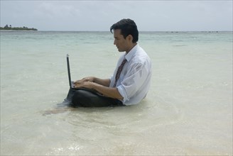 Hispanic businessman using laptop in water