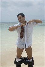 Hispanic businessman stripping at beach