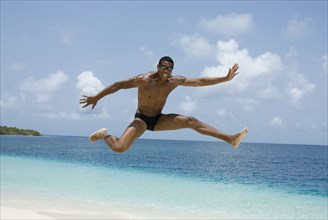 Hispanic man jumping at beach
