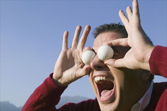 Hispanic man holding golf balls over eyes
