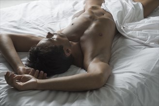 Nude Hispanic man laying in bed