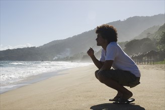 African man crouching at beach