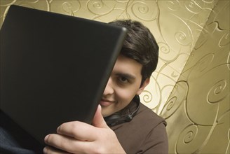 Hispanic man hiding behind laptop
