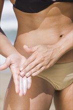 Hispanic woman applying sunscreen at beach