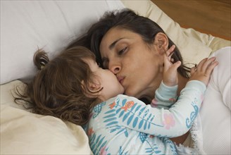 Hispanic mother kissing daughter in bed