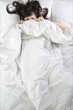 Mixed race woman peeking out from bed blankets