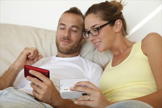 Caucasian couple laying in bed with cell phones