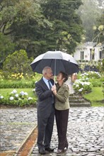 Hispanic couple standing together under umbrella