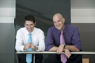 Hispanic businessmen leaning on railing together