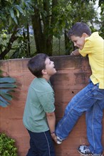 Hispanic boy helping friend climb wall