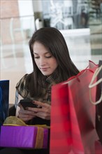 Hispanic woman with gifts text messaging on cell phone