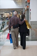 Senior Hispanic couple hugging and carrying shopping bags