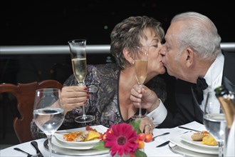 Kissing Hispanic couple toasting with Champagne in restaurant
