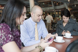 Hispanic business people text messaging on cell phones in cafe