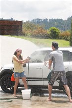 Playful Hispanic couple washing car together