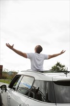 Hispanic man with arms outstretched standing in sun roof