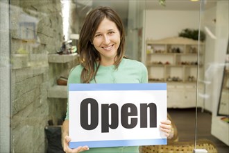 Hispanic woman holding open sign in shoe store