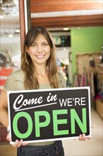 Hispanic woman holding open sign in store
