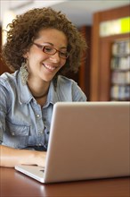 Hispanic woman using laptop in library