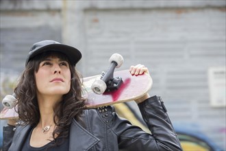Hispanic woman holding skateboard outdoors