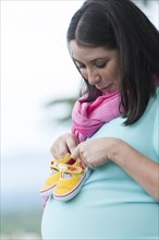 Pregnant Hispanic woman holding baby shoes