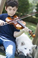Hispanic boy playing violin with dog