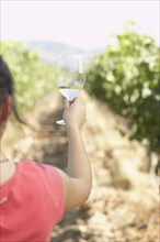 Hispanic woman holding glass of white wine in vineyard