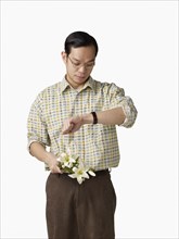 Asian man holding bouquet of flowers and checking watch