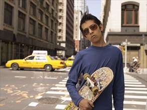 Indian man on city street holding skateboard