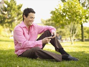 Man sitting in grass text messaging in park