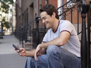 Man on front stoop text messaging on cell phone