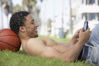 Young mixed race man with bare chest on grass with cell phone