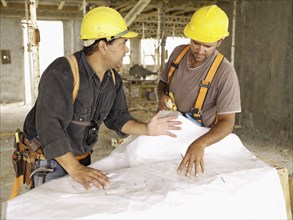 Hispanic workers looking at blueprints on construction site
