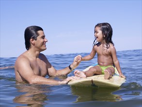 Hispanic father holding hands with daughter on surfboard