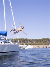 Hispanic man jumping into ocean from sailboat