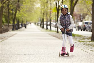 Mixed race girl riding on push scooter on sidewalk
