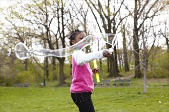 Mixed race girl making bubbles in park